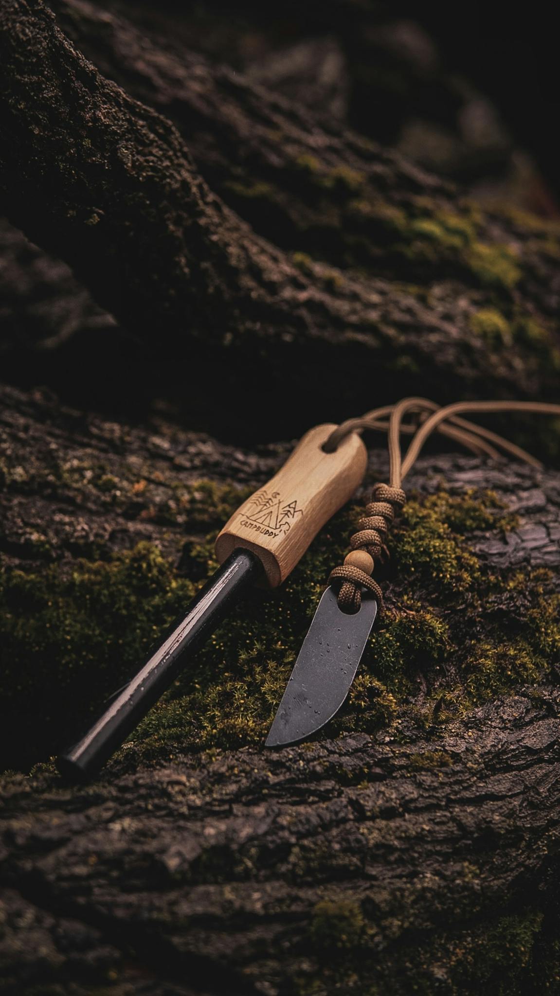 A flint and steel fire starter tool with wooden handle on mossy tree bark, ideal for outdoor survival.